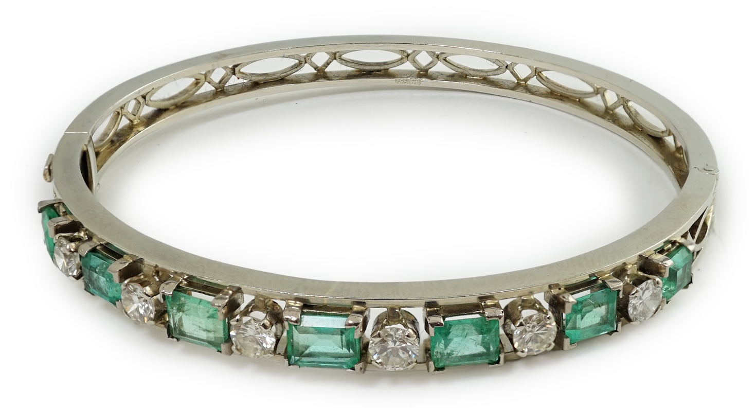 A modern 14k white gold, seven stone graduated emerald and six stone round cut diamond set hinged bangle